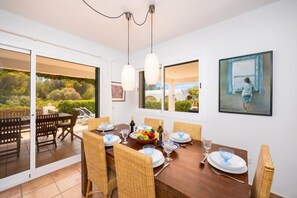 Un comedor con una mesa de madera, sillas de mimbre y vistas al exterior.