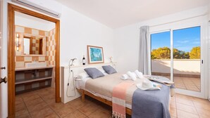 Un dormitorio con cama, mesita de noche, espejo, ventana y vistas al exterior.