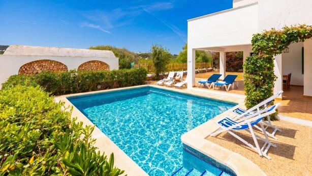 Una piscina con agua azul cristalina, rodeada de follaje y paredes blancas.