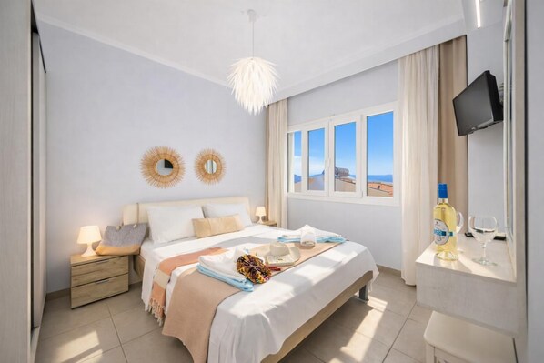 A bedroom with a bed, bedside tables, a TV, a window with a view, and a bottle of alcohol. - Villa Aurora - Three Bedroom Villa, Sleeps 6 (Mparmpati)