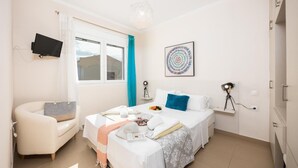 Hotellihuone, jossa on sänky, ty öpöytä, tuoli, televisio ja ikkuna, jossa on verhot.