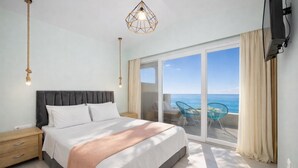 Une chambre à coucher comprenant un lit, des tables de chevet, une grande fenêtre donnant sur la mer et un luminaire au plafond.