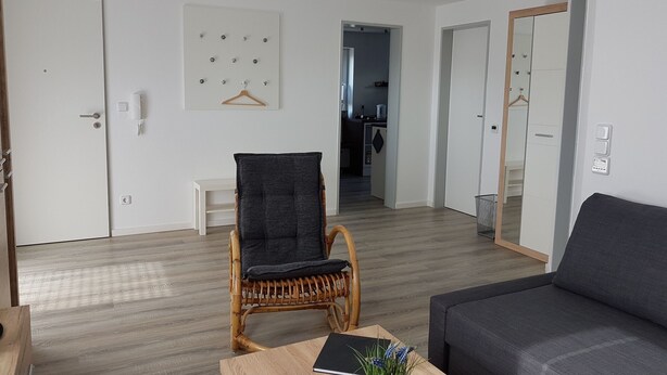 A modern living room with a sofa, a wicker chair, a wooden coffee table, and a kitchen in the background. - Apartment "Olsberg View Whg. B" with Mountain View, Shared Garden and Wi-Fi (Olsberg)