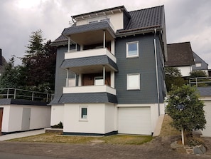 Un edificio residenziale a più piani con tetto piatto, un balcone al secondo piano e un portone garage.