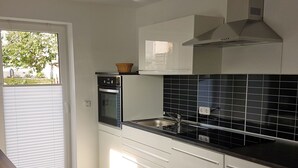A modern kitchen with a built-in oven, a microwave, a sink, and a window with blinds. - Apartment "Olsberg View Whg. B" with Mountain View, Shared Garden and Wi-Fi (Olsberg)