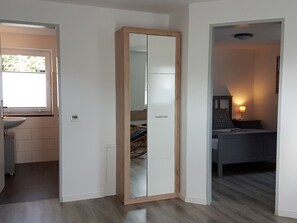 Quarto com um espelho grande, uma cama, uma mesa de cabeceira com abajur e uma janela.