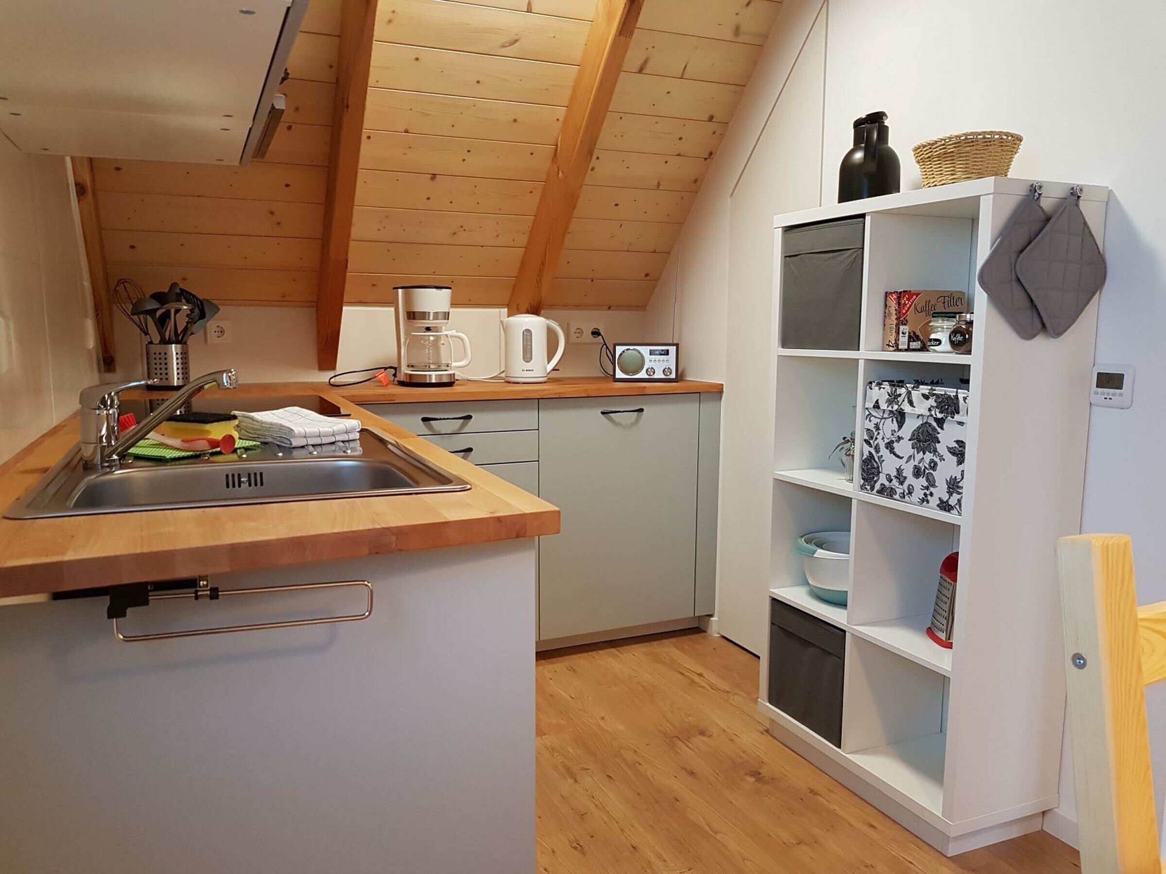 A kitchen with a wooden countertop, a sink, a coffee maker, a radio, and a shelf with kitchen items.
