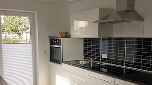 A modern kitchen with a built-in oven, a microwave, a sink, and a window with blinds. - Apartment "Olsberg Blick Whg.A" with Mountain View, Garden & Wi-Fi (Olsberg)