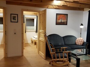 Een kamer met een houten plafond, een schommelstoel, een bank, een kleine tafel en een schilderij van een boom.
