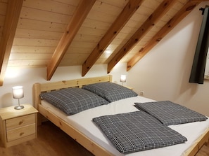 Een slaapkamer met een houten plafond, een bed met zwart-wit geruit beddengoed, een bedlampje en een houten nachtkastje met een lade.