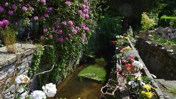 Um jardim com muro de pedra, um pequeno riacho e diversos vasos de plantas.