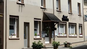 A multi-story building with a flat facade, multiple windows, and a covered entrance area with potted plants. - Room “Domaine du Chêne” (La Vôge-les-Bains)