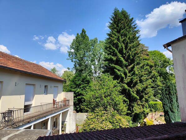 A building with a tiled roof, a balcony with chairs, and a large tree in the background. - Room “Domaine du Chêne” (La Vôge-les-Bains)