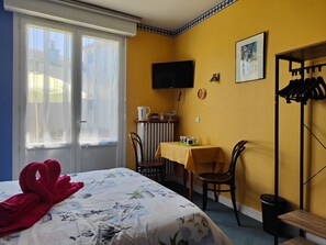 Una camera d'albergo con un letto, una scrivania, una sedia, una televisione e un appendiabiti.