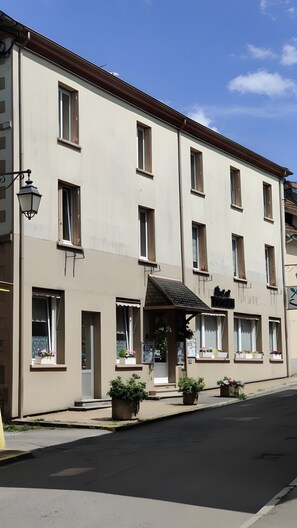 Un immeuble à plusieurs étages doté d’une façade sobre, de nombreuses fenêtres et d’un espace d’entrée abrité agrémenté de plantes en pot.