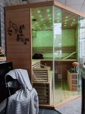 Una stanza con una porta scorrevole in vetro che dà su un'area sauna, una panca in legno e un piccolo armadietto di legno.