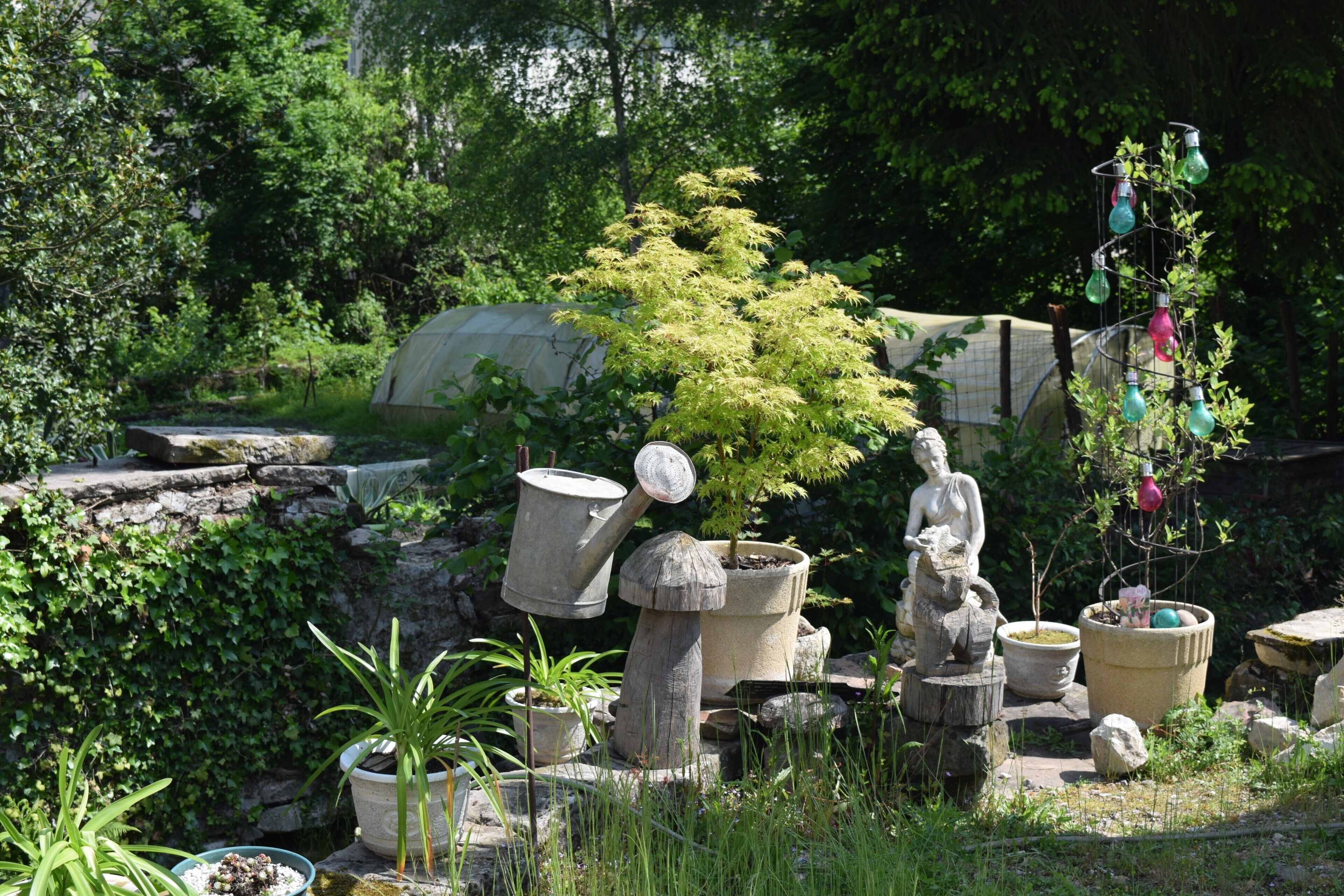 En have med krukkeplanter, en stenstatue og en metalskulptur.