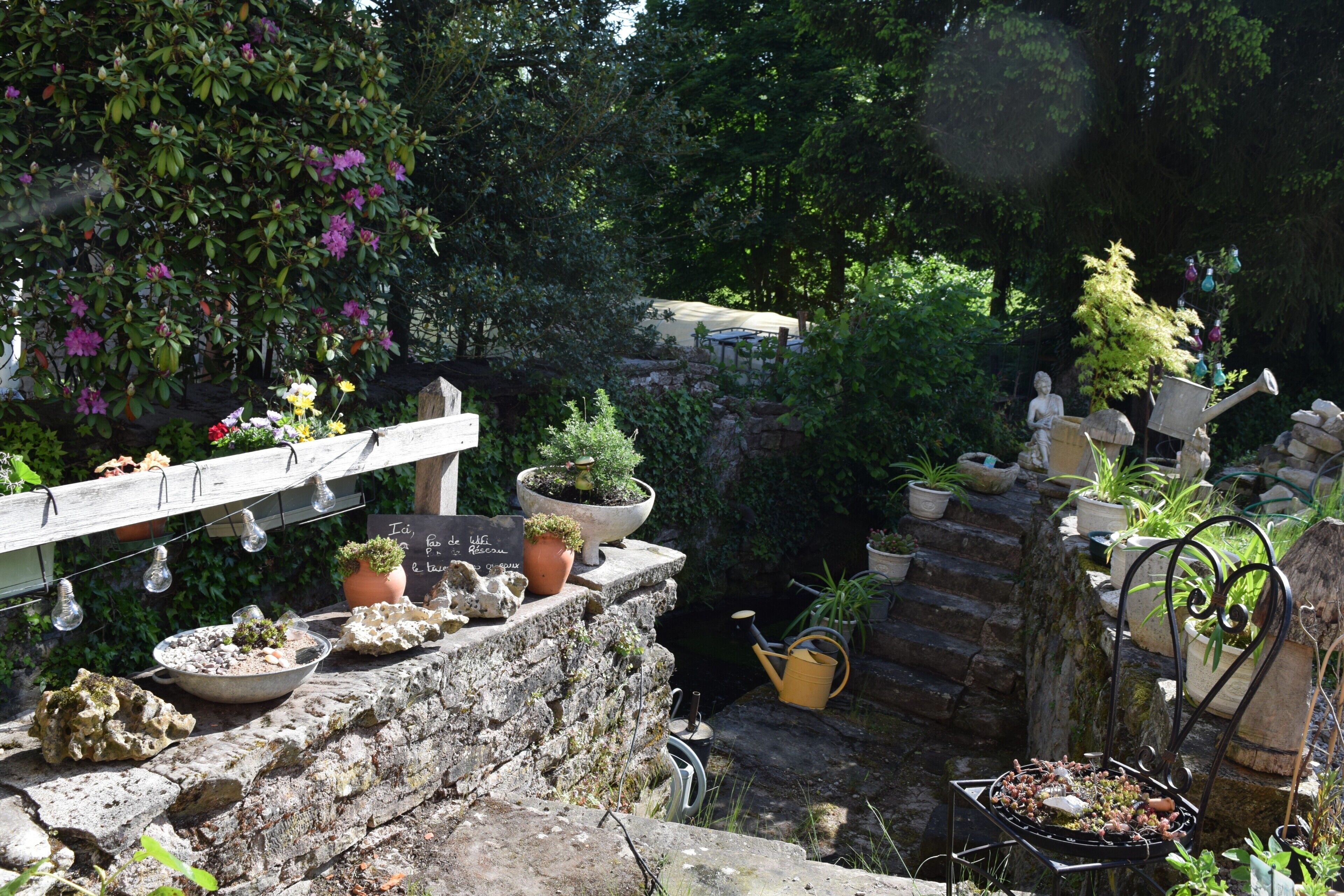 A garden with potted plants, a stone wall, and a metal chair.
