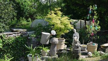 Un jardin agrémenté de plantes en pot, d’une statue en pierre et d’une sculpture en métal.