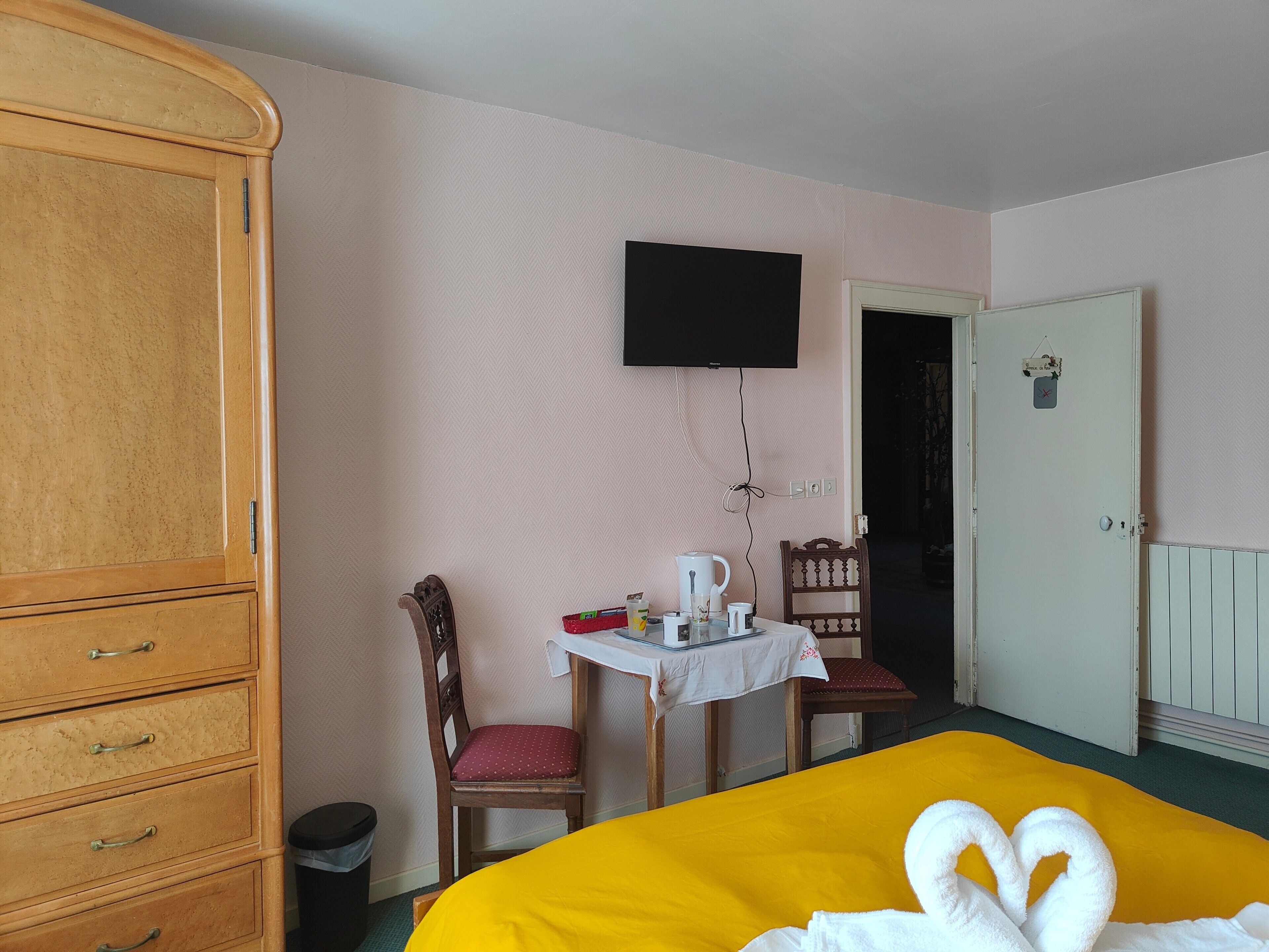 A hotel room with a bed, a wooden wardrobe, a television, a table with a chair, and a door.