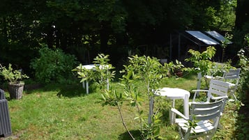 Un jardin avec des chaises et des tables blanches, entouré de verdure et agrémenté d’une serre.