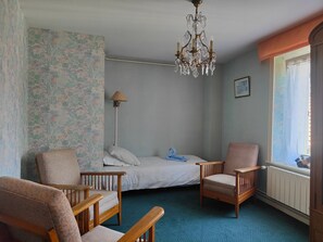 Una camera da letto con un letto, due sedie in legno, una lampada da terra, un lampadario, una finestra con tende e carta da parati a motivi floreali.