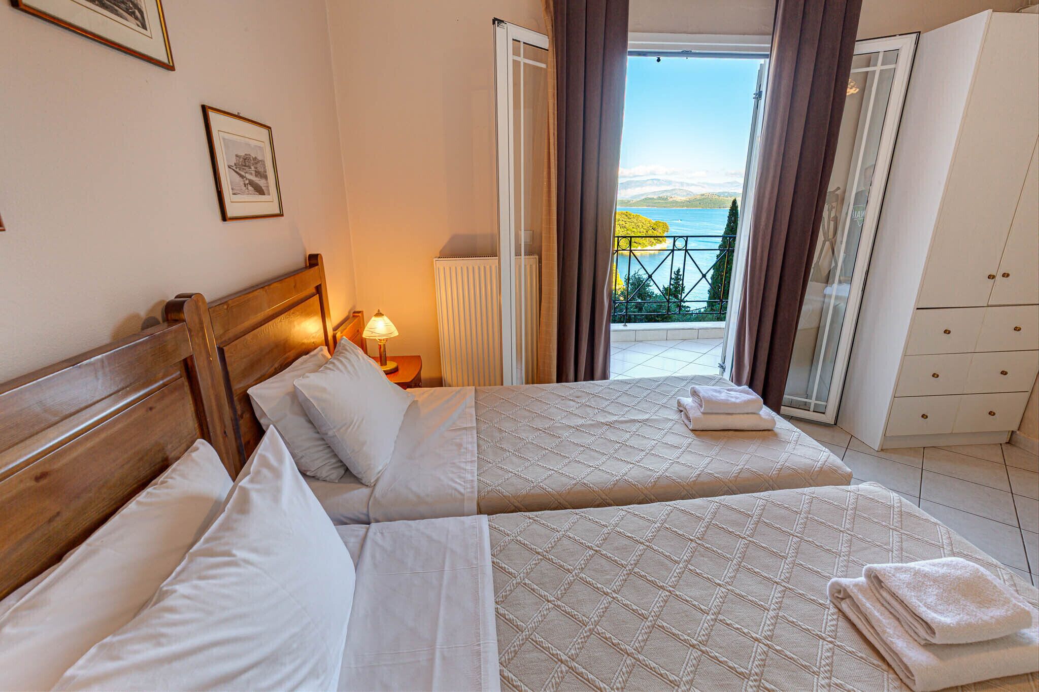 A hotel room with two beds, a view of the sea, and a balcony with a railing.