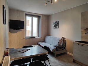 Et kompakt værelse med et tekøkken, et spiseområde, en sofa og et fjernsyn ophængt på væggen.