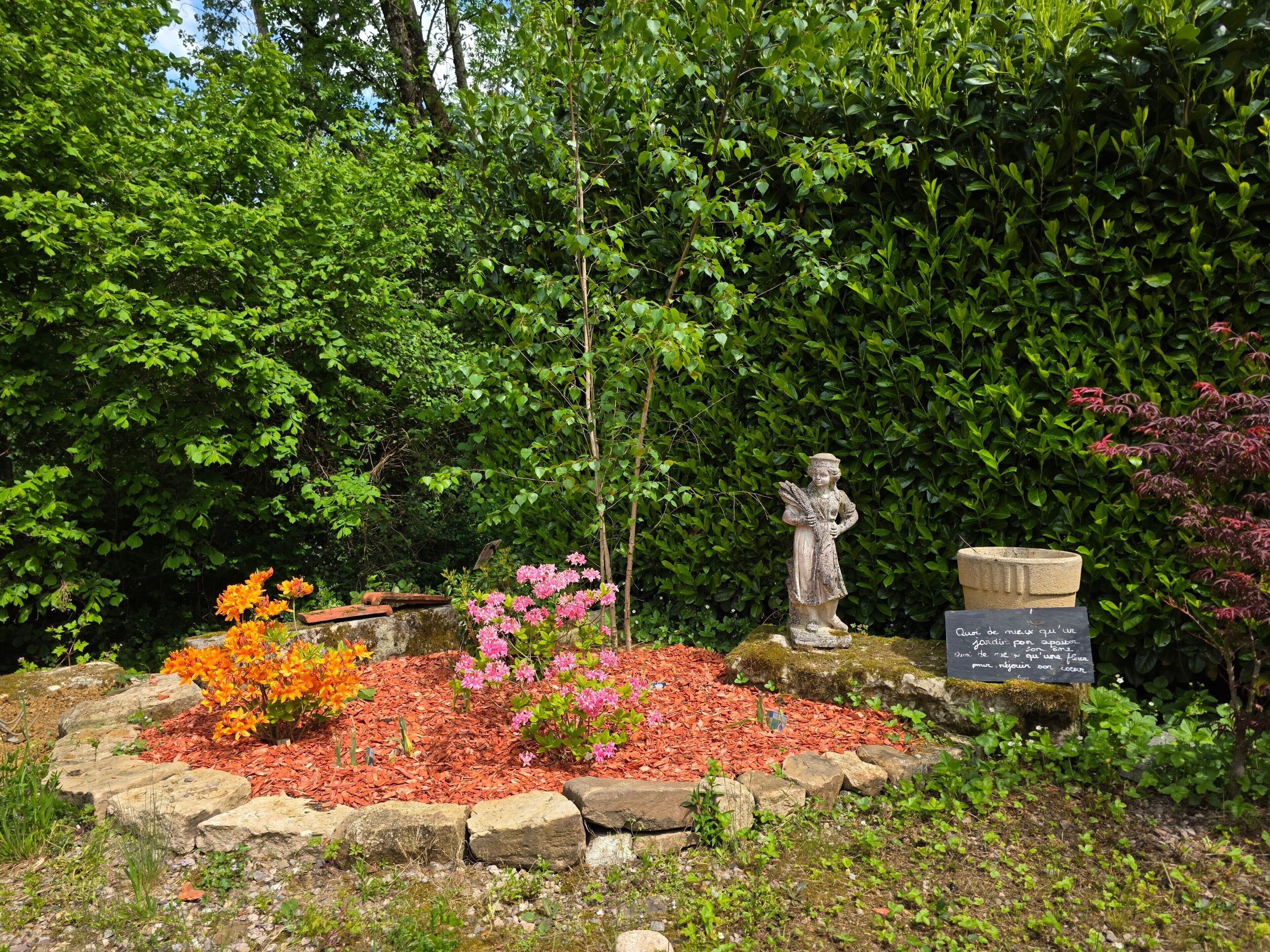 A garden with a statue, a stone plaque, and various plants.