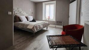 A bedroom with a bed, a window, a radiator, a chair, and a table.