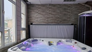 A hot tub with a control panel, a window with a view of the outside, and a tiled wall.