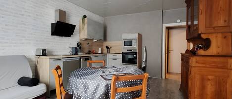 Ein kompakter Wohnraum mit Küchenzeile, einer Essecke mit Tisch und Stühlen, einer Couch und einem Holzkasten.