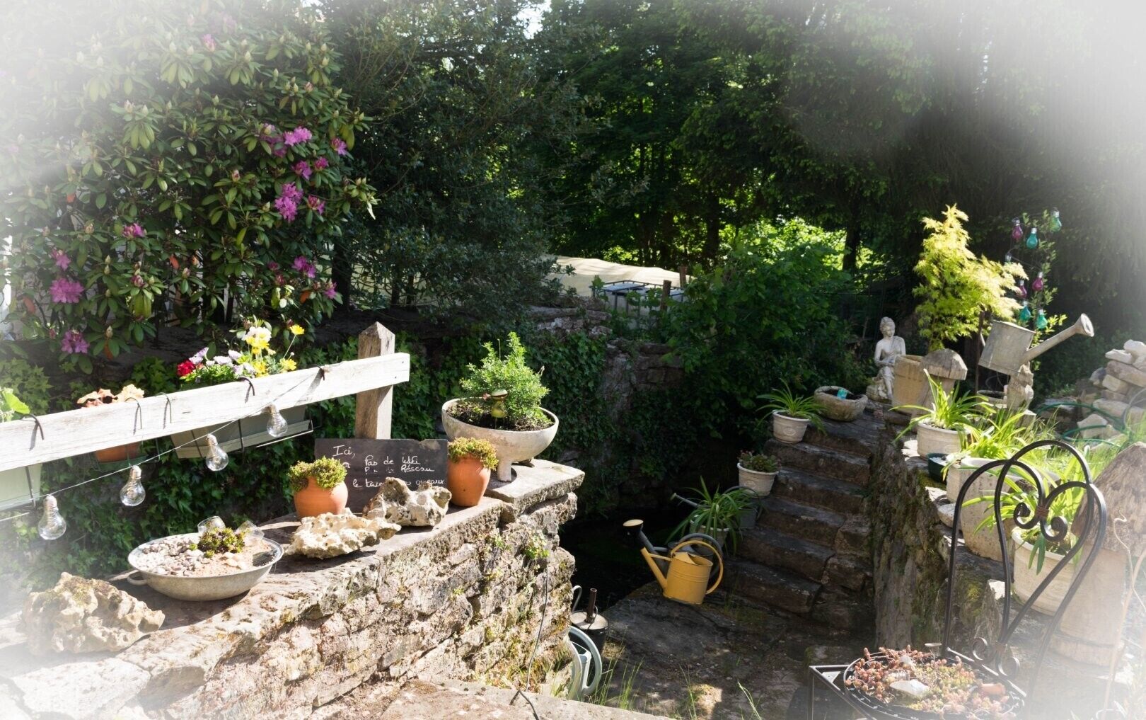 Un jardin agrémenté de plantes en pot, d’un mur de pierre et d’une clôture en bois.