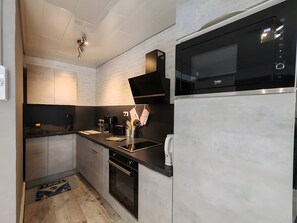 A modern kitchen with a built-in microwave, oven, and dishwasher, featuring a minimalist design and light-colored cabinetry. - La diligence de la poste – Furnished T2 at Domaine Du Bouleau with Air Conditioning (La Vôge-les-Bains)