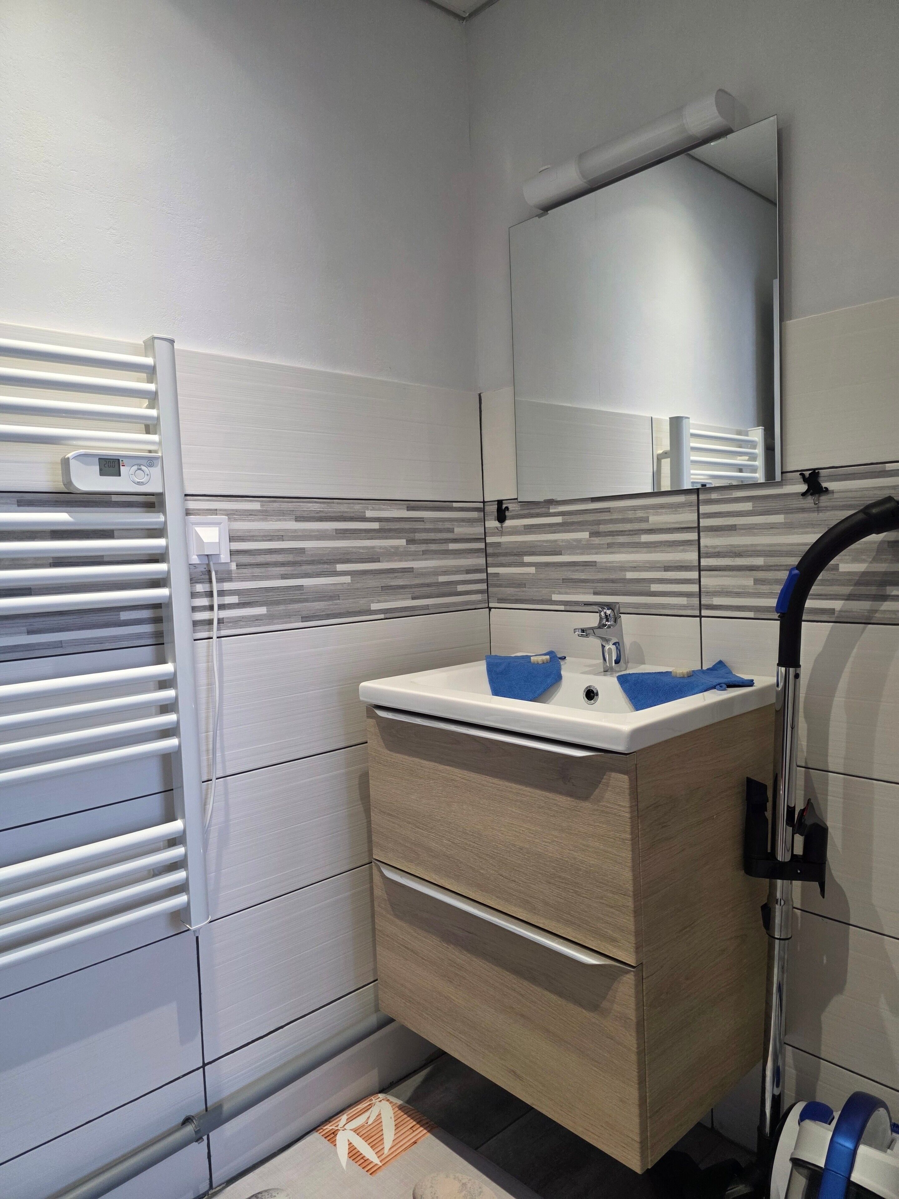A modern bathroom with a white vanity, a mirror, a towel rack, and a shower area.