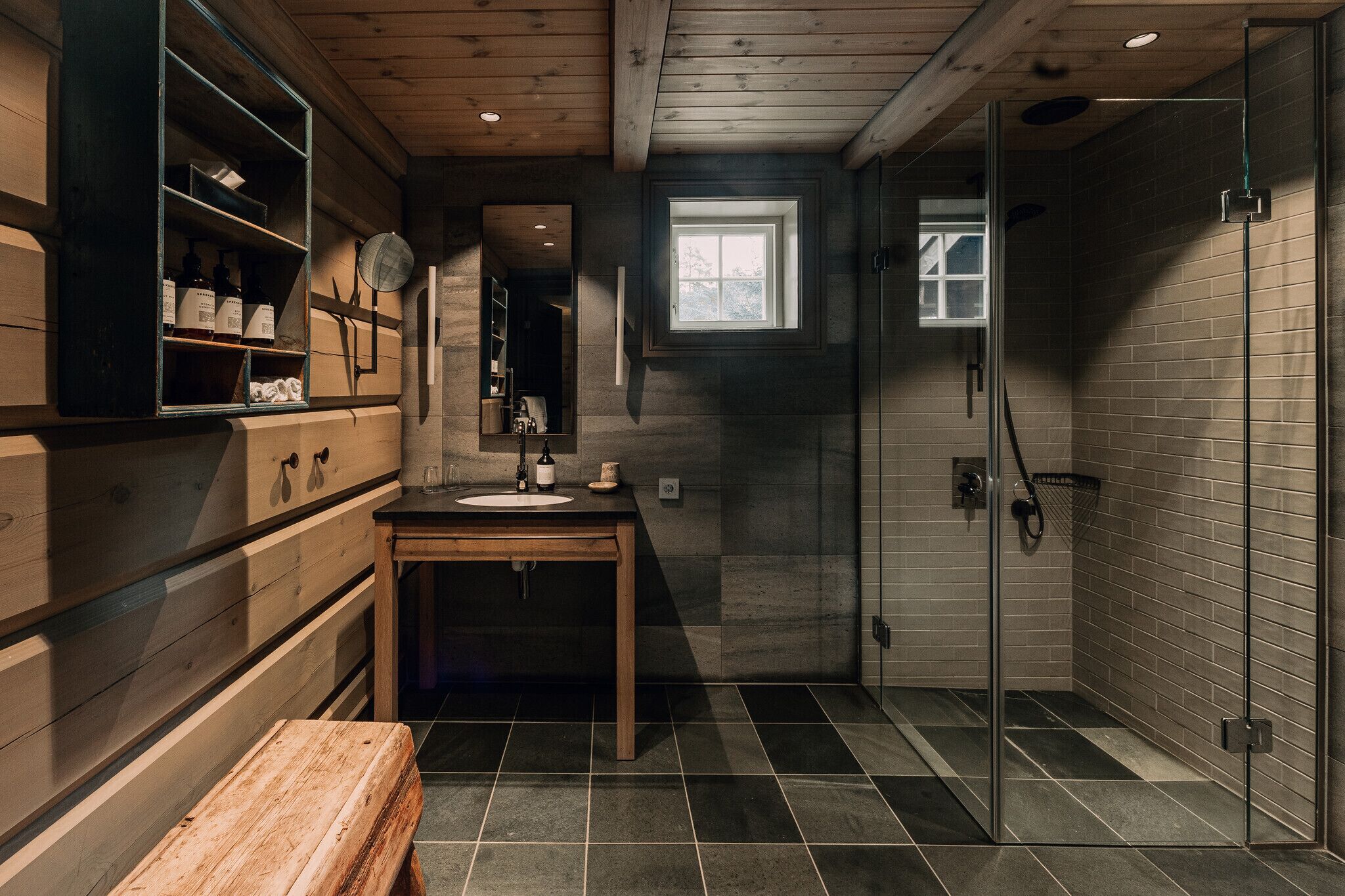 Un baño moderno con tocador de madera, cabina de ducha de vidrio y una ventana pequeña que deja entrar luz natural.