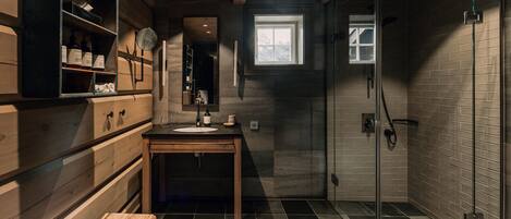 Un baño moderno con tocador de madera, cabina de ducha de vidrio y una ventana pequeña que deja entrar luz natural.