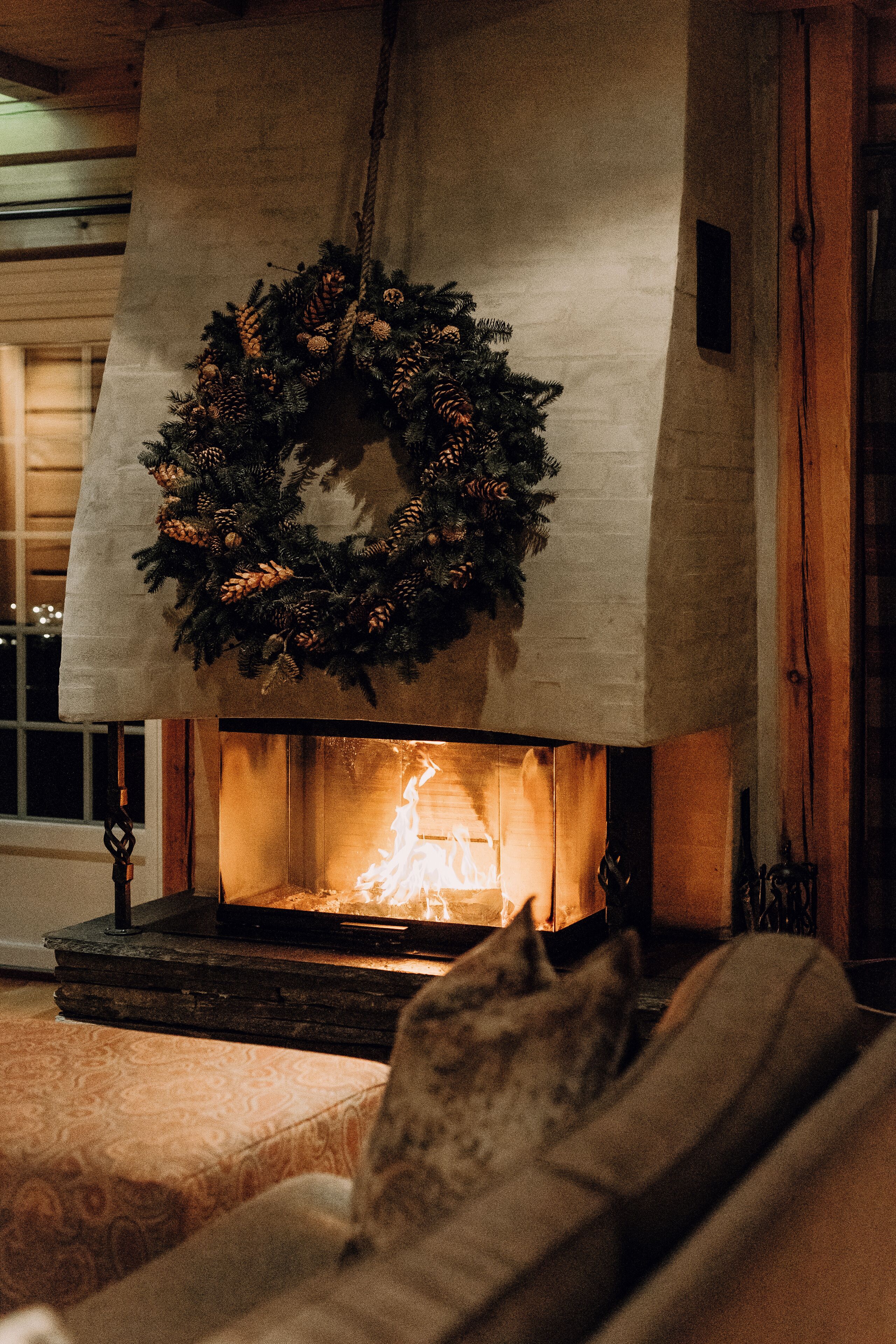 A fireplace with a wreath, a couch with cushions, and a window in the background.