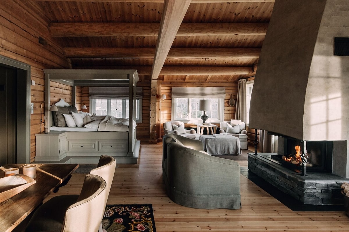 Interior acogedor de una cabaña de troncos con chimenea, piso de madera y una zona de estar cómoda.