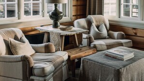 A cozy cabin-style room with a wooden ceiling, a sofa, a chair, a small table, and a window with curtains. - Storfjord Hotel (Ålesund)