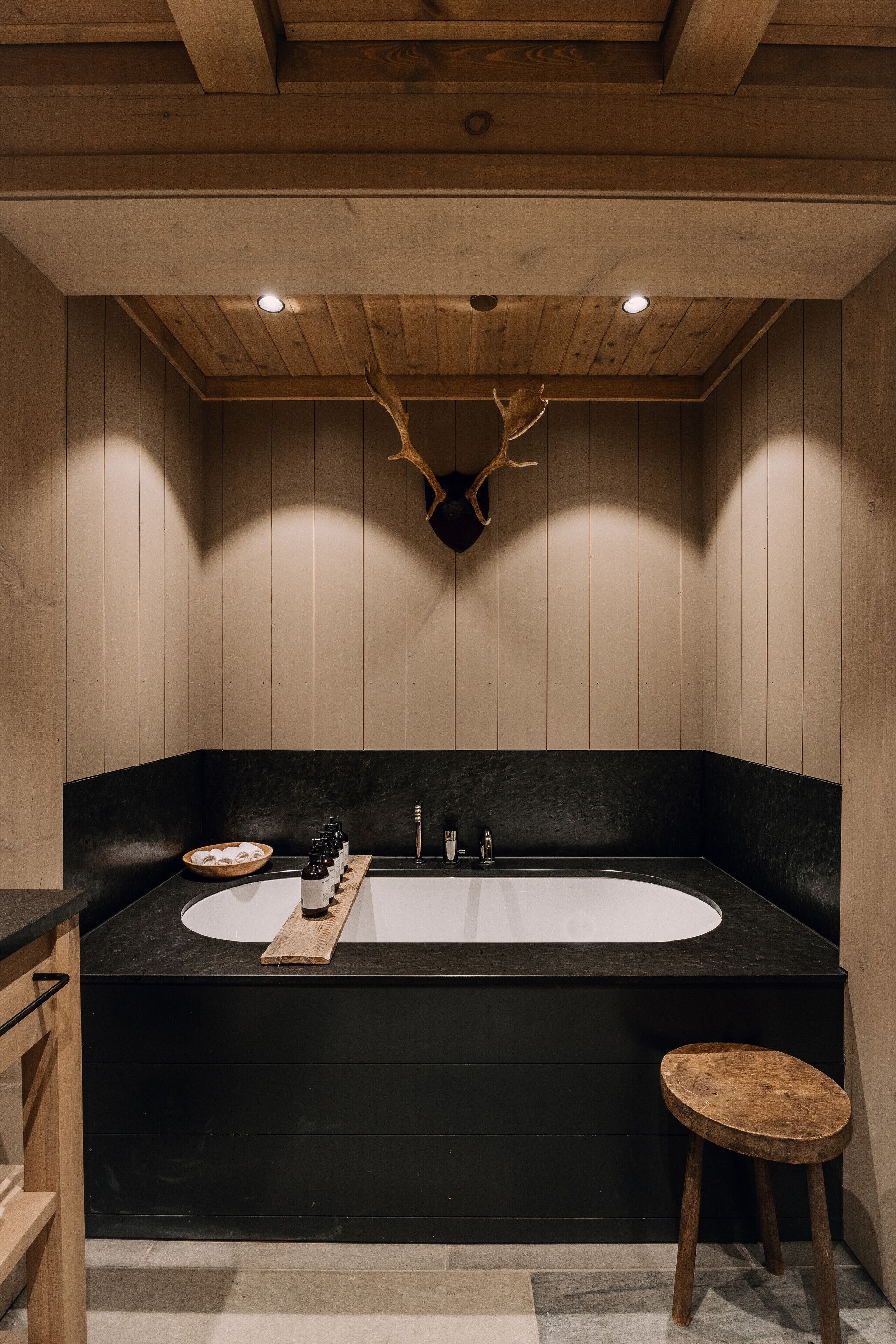 A modern bathroom with a black bathtub, wooden accents, and a deer head mounted on the wall.