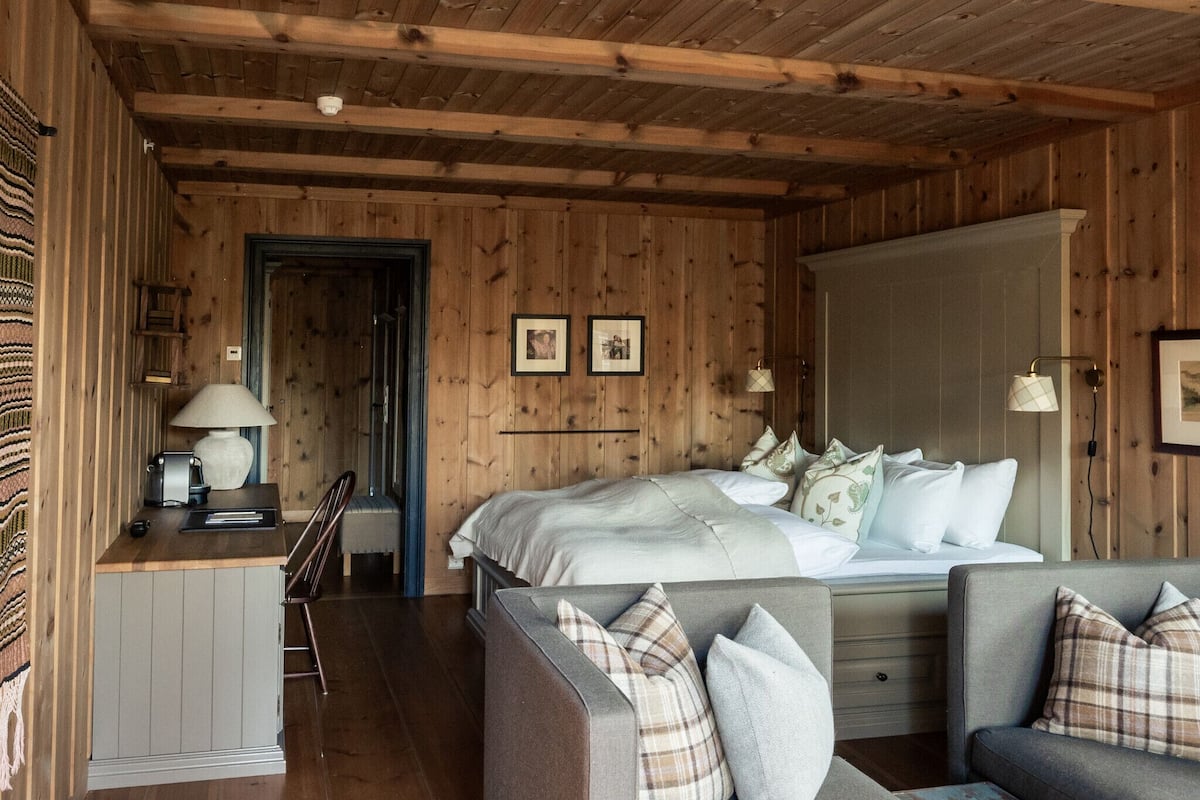 Un dormitorio de cabaña de madera con cama, mesitas de noche y un sofá.