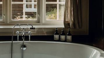 A bathroom with a freestanding bathtub, a window with curtains, and a shelf with toiletries.