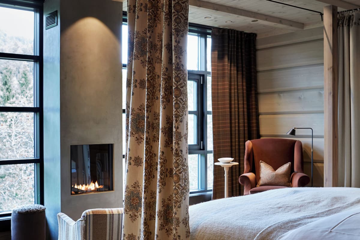 Un dormitorio con una cama grande, una silla, una mesita y una chimenea.