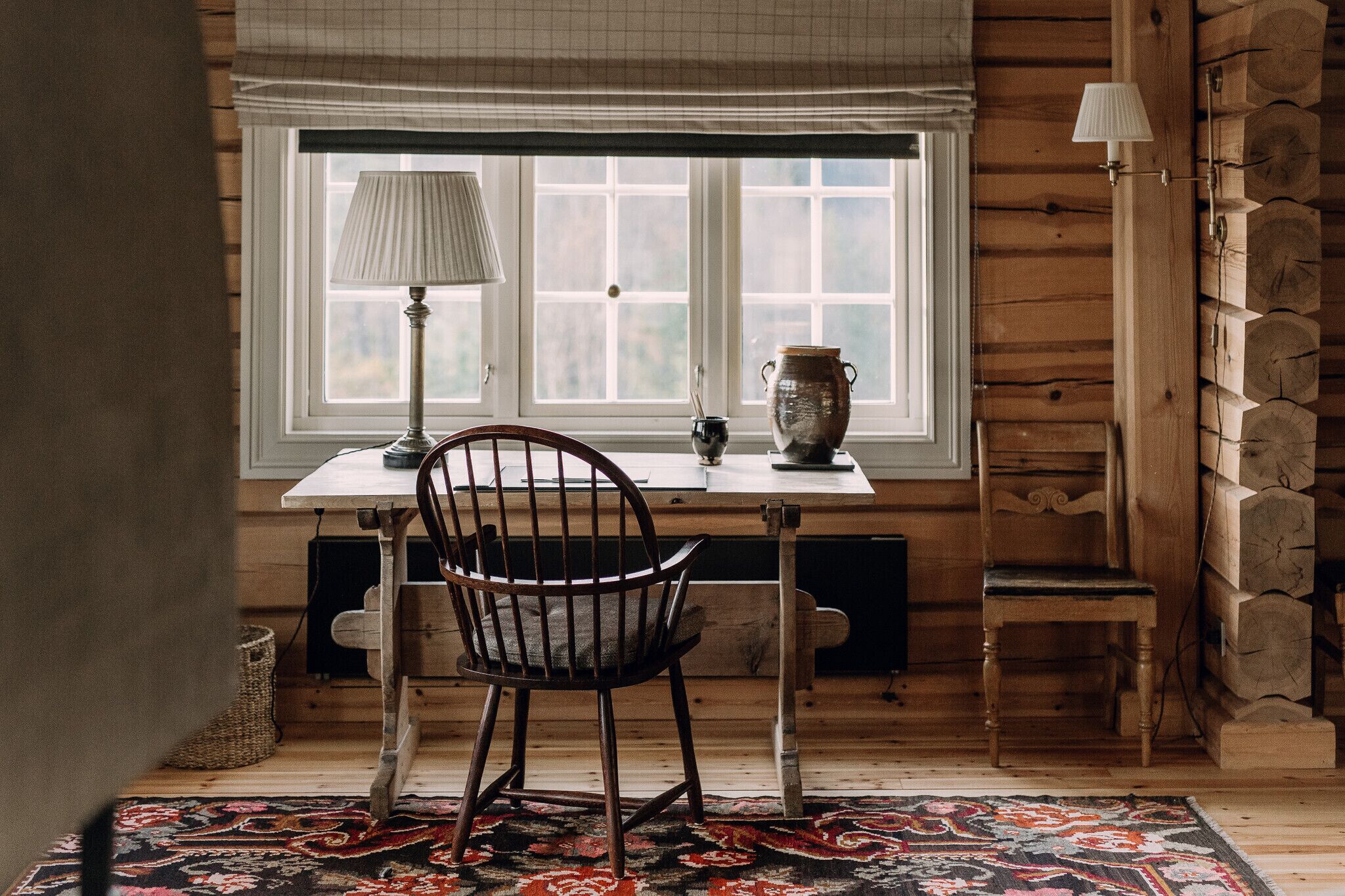 Una habitación acogedora con una mesa de madera, una silla, una lámpara y una ventana con vistas.