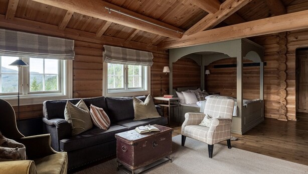 A log cabin interior with a dark leather sofa, a plaid armchair, and a vintage trunk as a coffee table. - Storfjord Hotel (Ålesund)