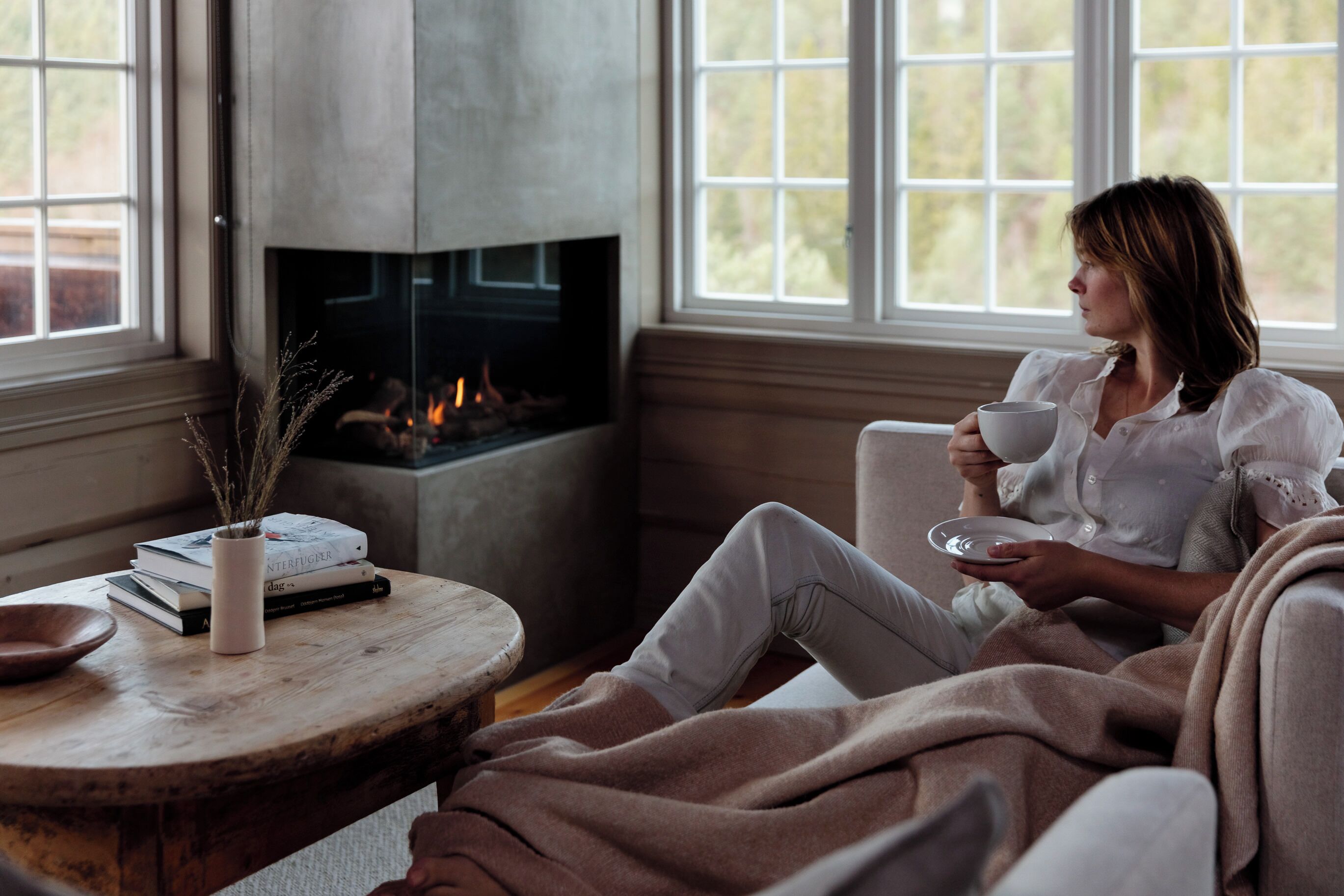 A cozy room with a fireplace, a window with a view, and a table with books and a vase.