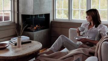 A cozy room with a fireplace, a window with a view, and a table with books and a vase.