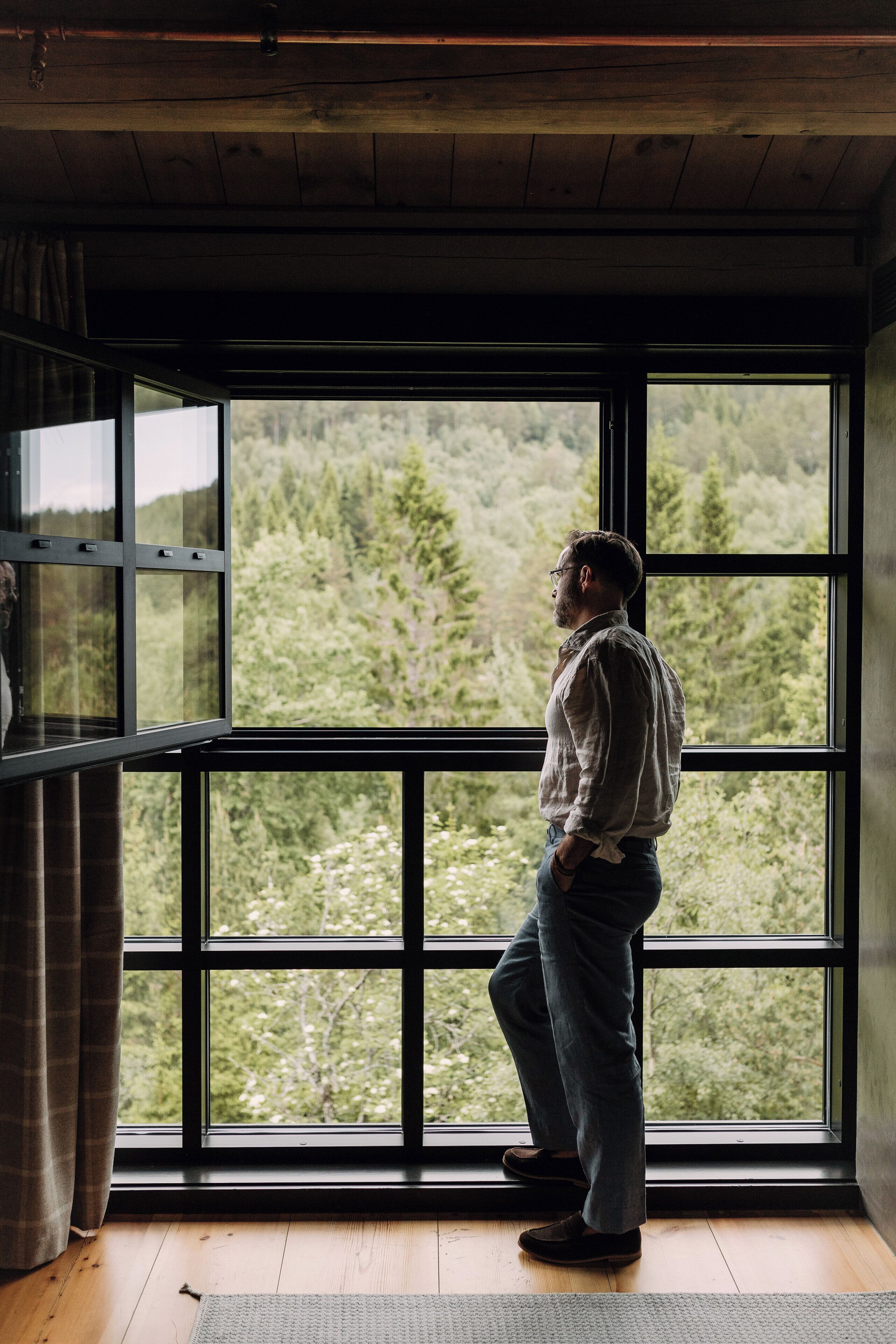 A person standing by a large window with a view of a forest.