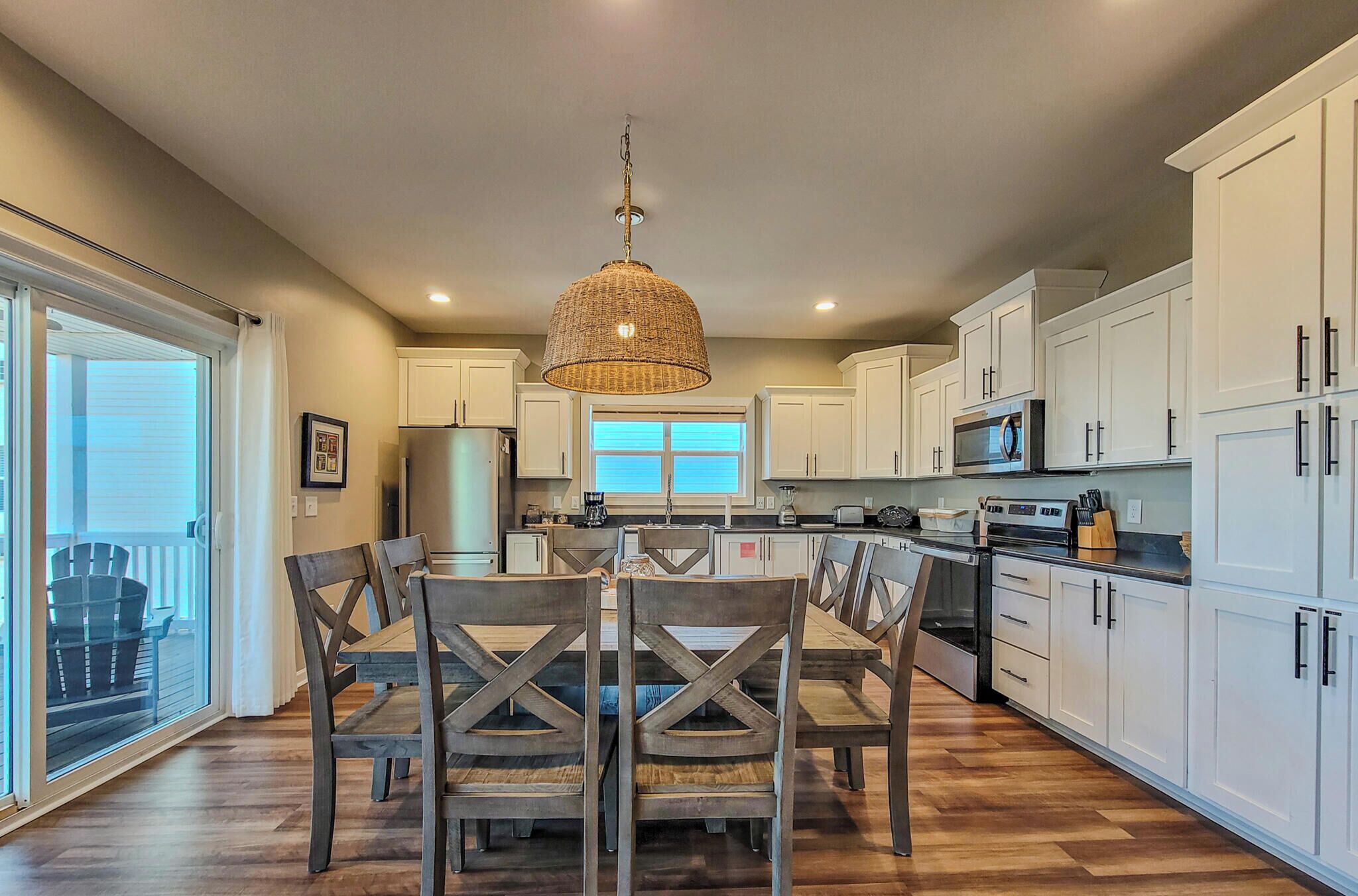 A modern kitchen with white cabinets, a dining table with chairs, and a hanging light fixture.